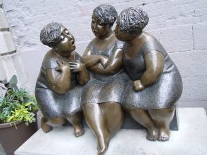 Statue intitulée Les Chuchoteuses où trois femmes sont en échange verbal et en totale attention
